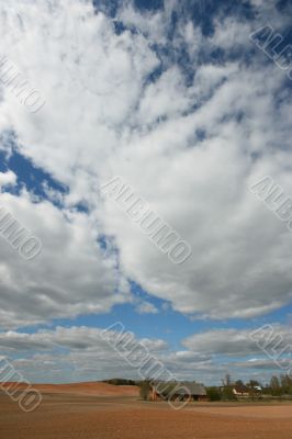 Country house in plough-land under cloudy sky in spring