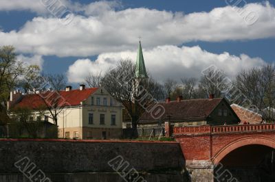 Church, houses, and bridge in sunny day with clouds