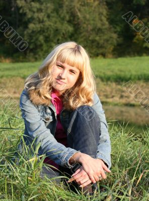young blond woman is sitting on a grass
