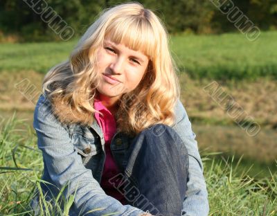 young blond woman is sitting on a grass
