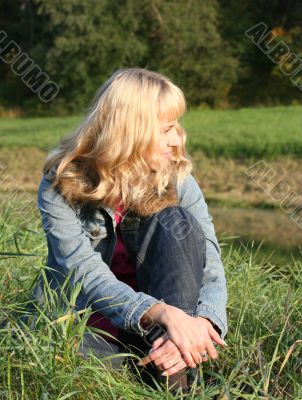 young blond woman is sitting on a grass