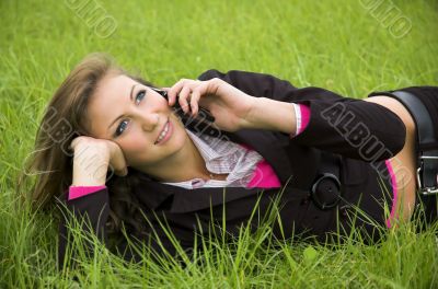 The girl speaks by phone laying on a green grass