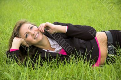 The girl speaks by phone laying on a green grass