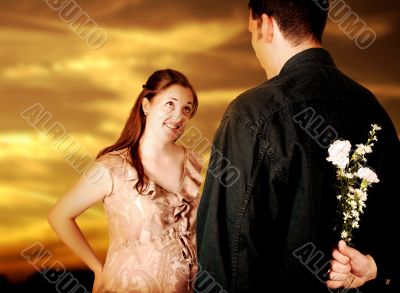 couple at sunset - guy hiding flowers from her