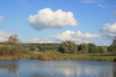 Cloudy sky over yellow autumn forest and pond