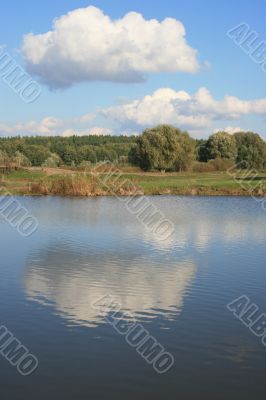 Cloudy sky over yellow autumn forest and pond