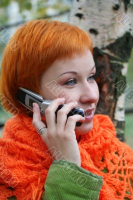 young red-haired woman in red scarf is talking in mobile-phone