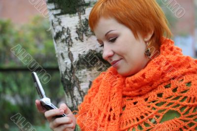 young red-haired woman in red scarf is sms in mobile-phone