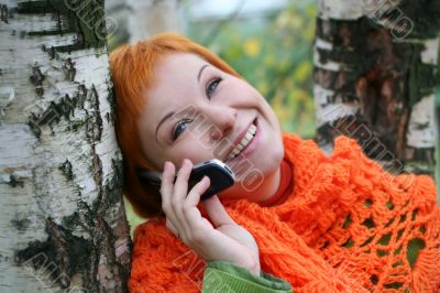 young red-haired woman in red scarf is talking in mobile-phone
