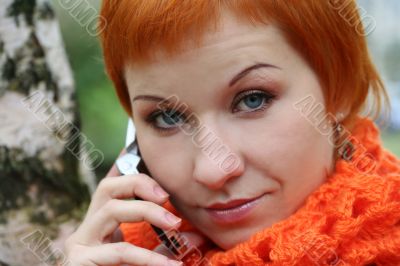 young red-haired woman in red scarf is talking in mobile-phone