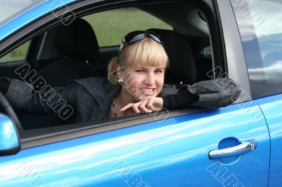 young blond woman in a blue car. She is smiling happy