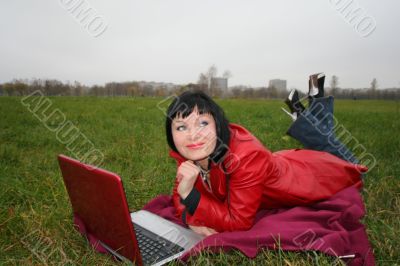 black head woman is laying on a plaid in park grass with notebook