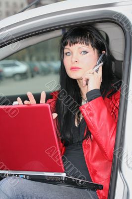 woman is calling by mobile phone and working at laptop in a car