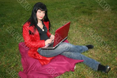 black head woman is sitting on a plaid in park grass with notebook