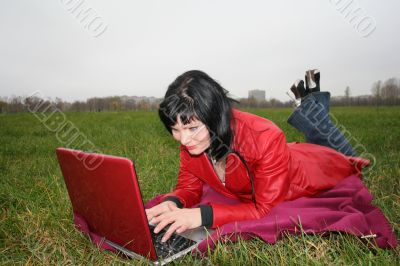black head woman is laying on a plaid in park grass with notebook