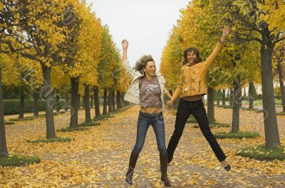 Two girls jump in autumn park