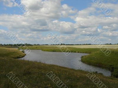 wide summer field with river uder cloudy blue sky