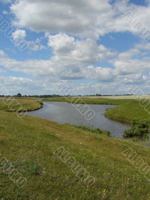 wide field with river uder cloudy deep blue sky