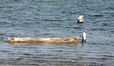 African man standing in water und pulling a boat