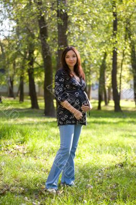 Pregnant woman in blue jeans saunter in park