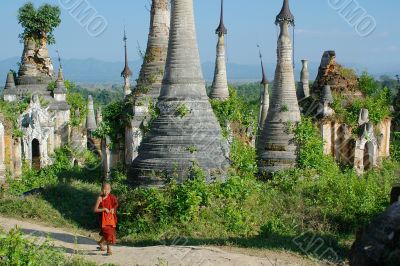 young monk walkng between stupas