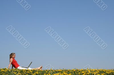 Girl relaxing with laptop in flowering field
