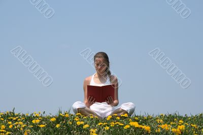 Young woman reading a book in a flowering field