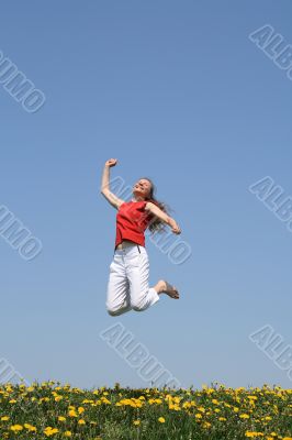 Smiling happy girl jumps in flowering field