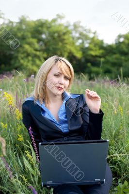 Contented businesswoman with pedicle in a mouth sitting on grass