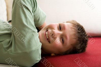 Happy teenager lie on red sofa at home