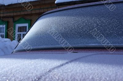 The car covered with frost, against the old wooden house.
