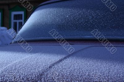 The car covered with frost, against the old wooden house.