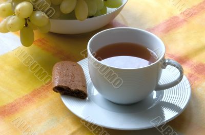 Cup of tea with a piece of biscuit and grapes.