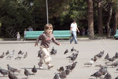 Beautiful girl running at city square and pigeons