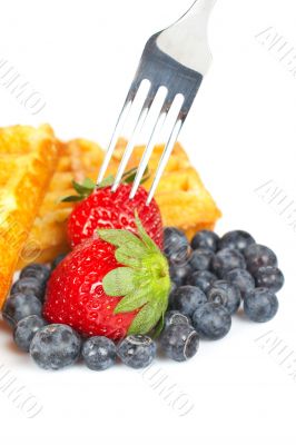 Waffles, blueberries and the fork pricking the strawberry