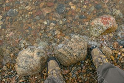 Legs in hiking boots on stone shore