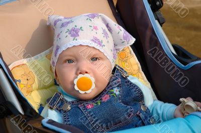 Little girl with baby`s dummy sit in carriage.