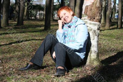 red haired woman is sitting near tree
