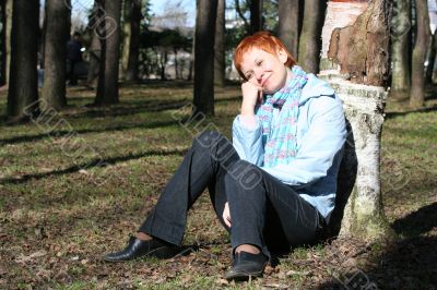 red haired woman is sitting near tree