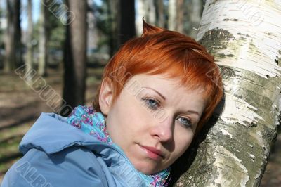 red haired woman is sitting near tree
