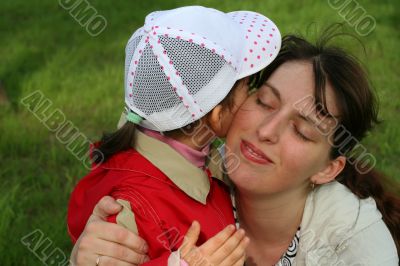 little girl with her mother in the spring park kissing