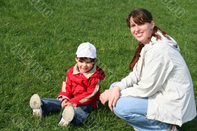 little girl with her mother in the park sitting on green grass
