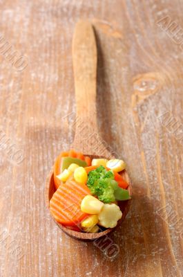 cooked carrots sweet corn and broccoli in a wooden spoon