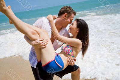 hunky caucasian man carrying gorgeos girl on the beach