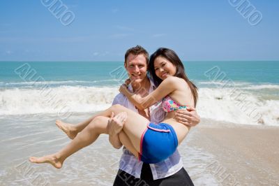hunky caucasian man carrying gorgeos girl on the beach