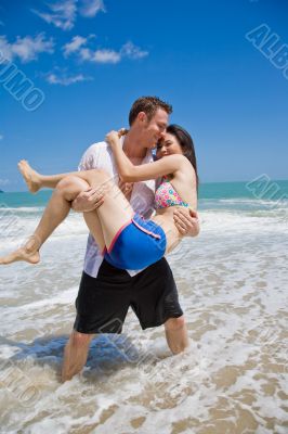 hunky caucasian man carrying gorgeos girl on the beach