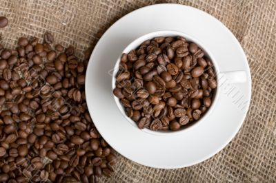 Cup with freshly roasted coffee beans on sackcloth