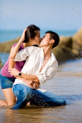 loving young couple kissing while squating by the beach