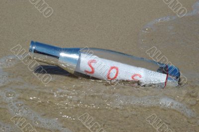 Message in a bottle with SOS signal lying in surf