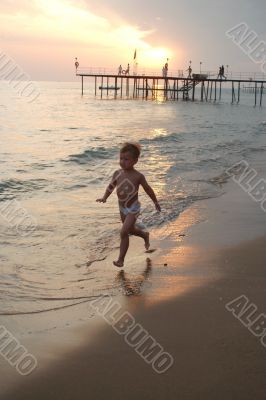 happy young boy running on the beach at sunset